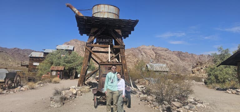 Two smile by a historic Hamm’s Beer tower in a Nevada desert ghost town near Las Vegas—perfect for ATV tours and ghost town sightseeing.