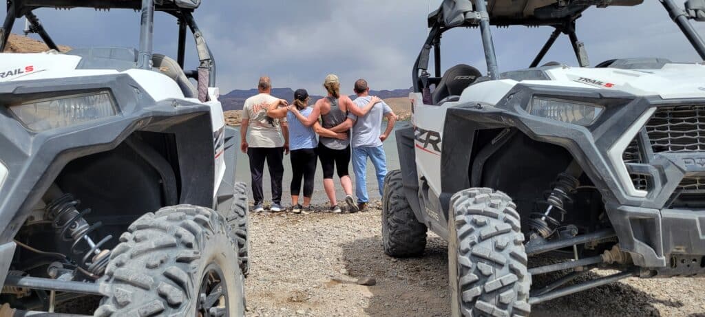 Five friends embrace between two ATVs in Nevada’s desert near Las Vegas, ready for a thrilling RZR off-road adventure.