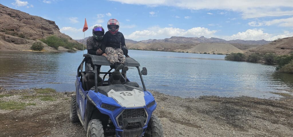 Two adventurers in helmets atop a blue RZR enjoy an ATV tour by the Colorado River near Las Vegas, Nevada’s scenic hills.