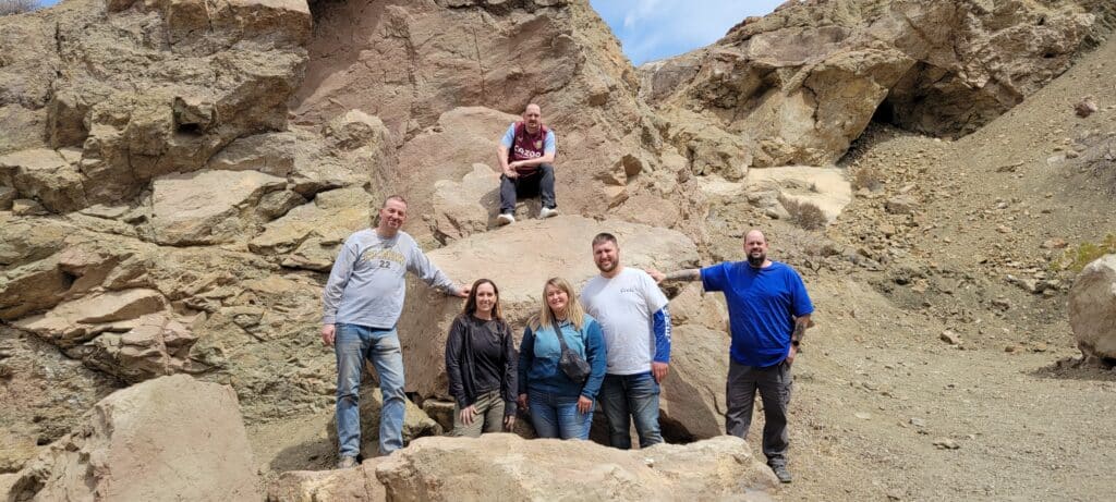 Six friends pose among Nevada rocks near the Colorado River during a Las Vegas RZR off-road ATV tour under partly cloudy skies.