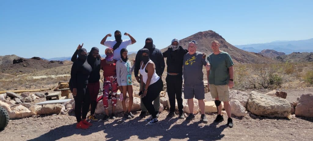 Ten friends smile and pose on rocky Nevada terrain near the Colorado River after an exciting Las Vegas ATV tour adventure.