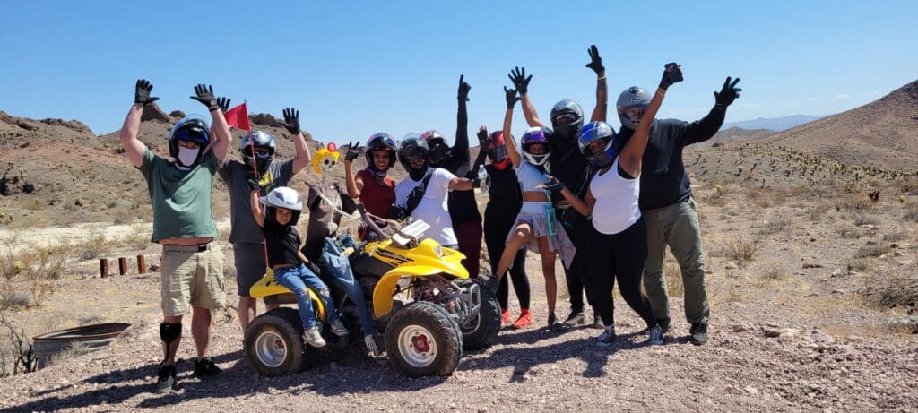 Adventure seekers in helmets pose by a yellow ATV on a Nevada desert tour near the Colorado River outside Las Vegas.
