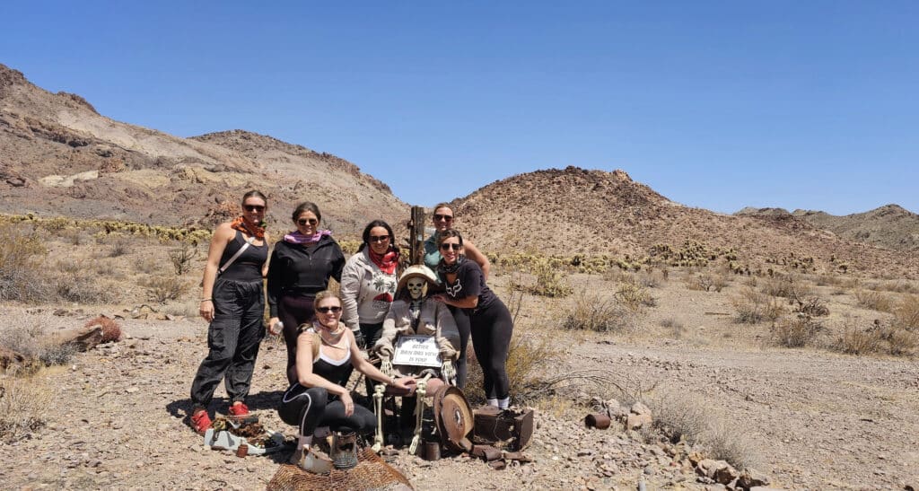 Seven friends pose near Las Vegas in Nevadas rocky desert with a skeleton at Area 51, perfect for ATV tours & off-road adventures!.