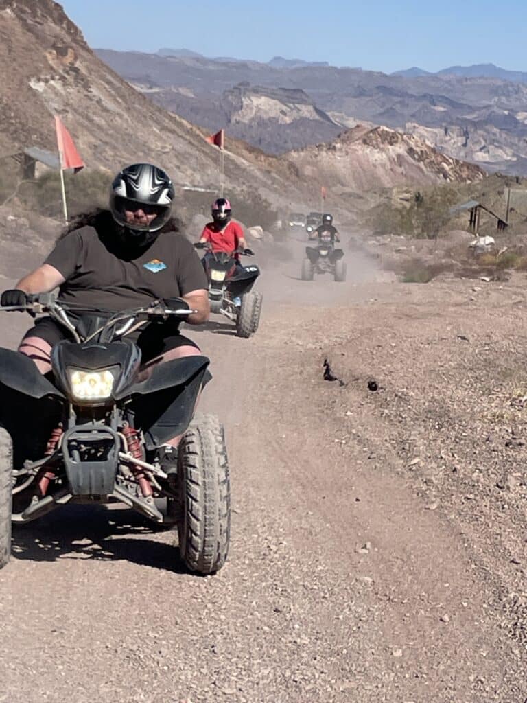 Three riders enjoy an ATV tour near Las Vegas, Nevada, cruising dusty desert trails with red flags and helmets for safety.