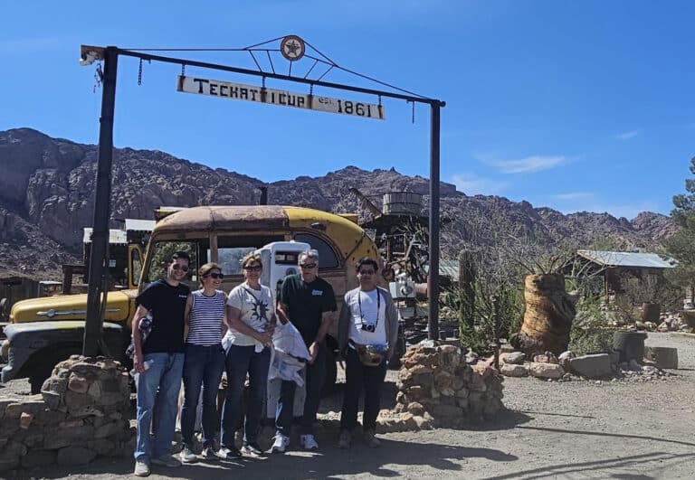 Five friends smile under the Techatticup sign at Nevadas historic ghost town near Las Vegas and the Colorado River.