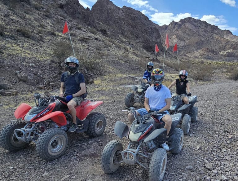 Adventurers on an ATV tour near Las Vegas ride RZR vehicles with red flags through Nevada desert trails by the Colorado River.