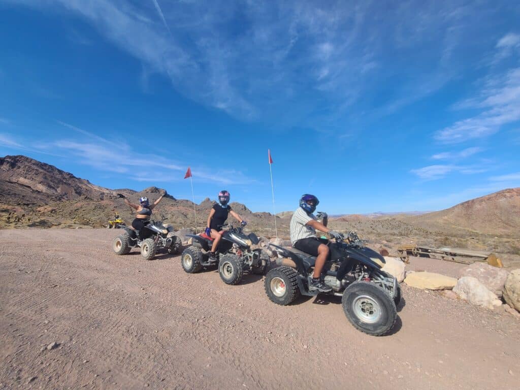 Riders in helmets enjoy a thrilling Las Vegas ATV tour on a desert trail near the Colorado River, red flags flying high.