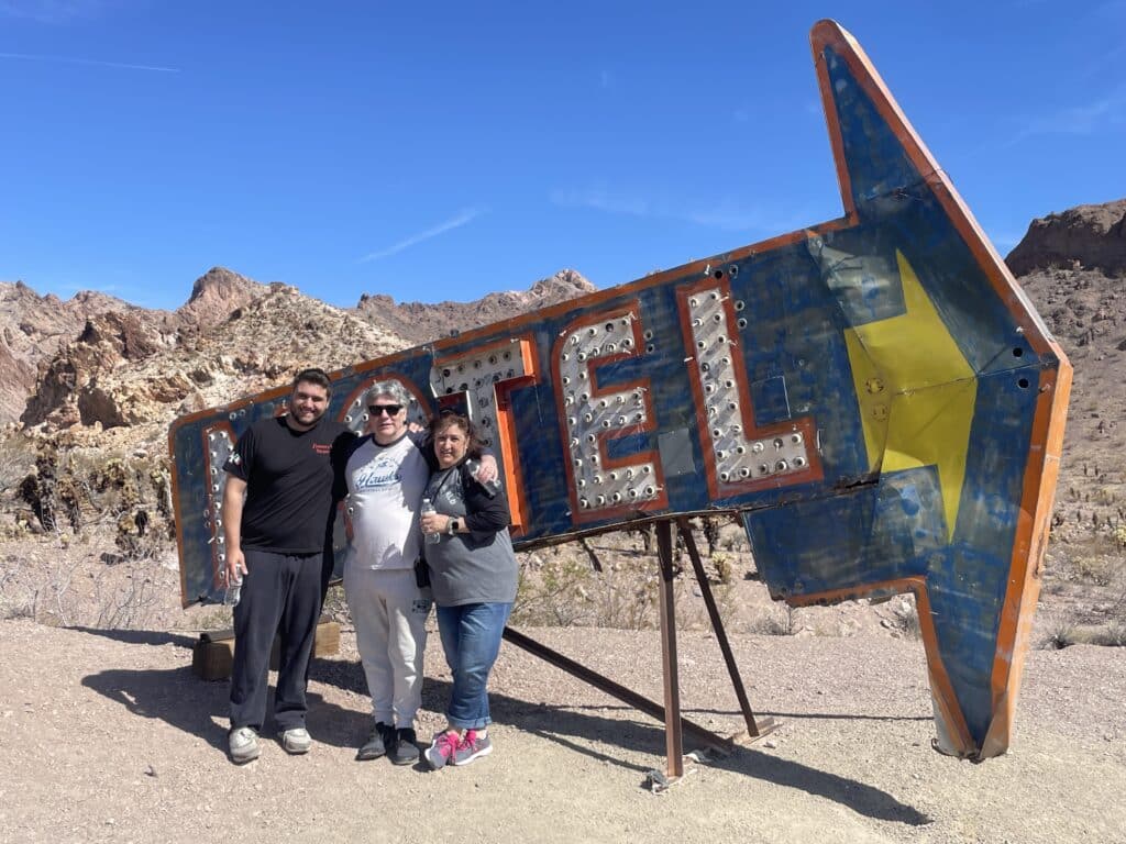 Three friends smile by a vintage MOTEL sign in the Nevada desert near Las Vegas, perfect for Ghost Town tours and ATV adventures.