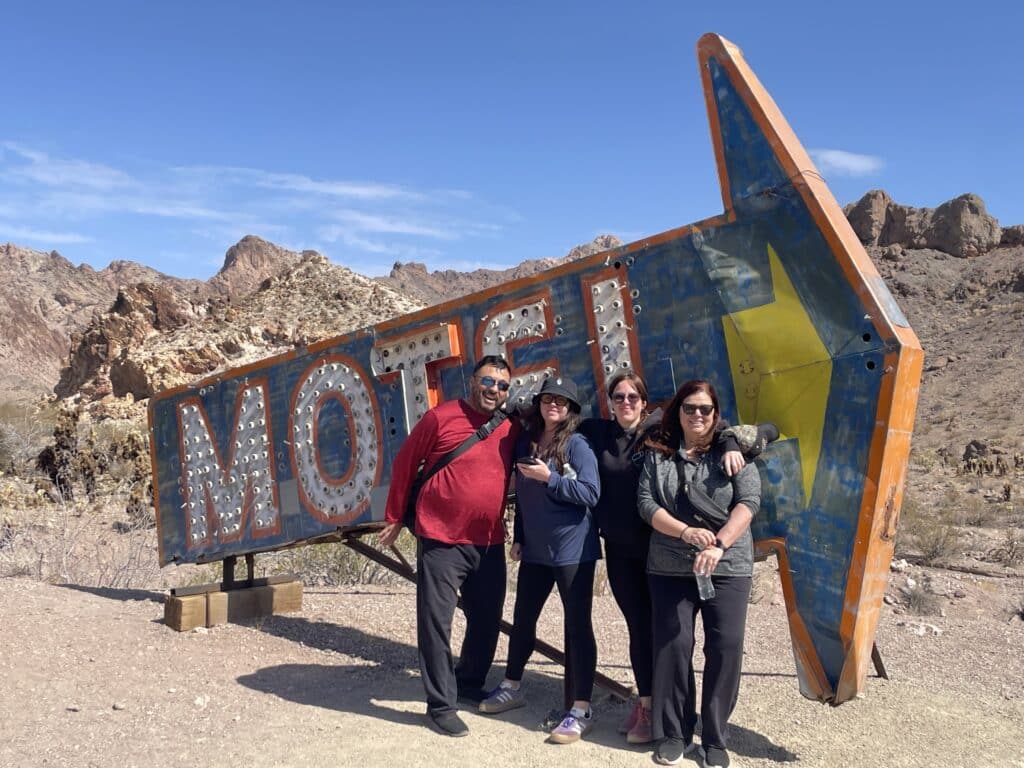 Four friends smile by a vintage MOTEL sign in Nevada’s desert near Las Vegas, perfect for RZR off-road rides or Ghost Town tours.