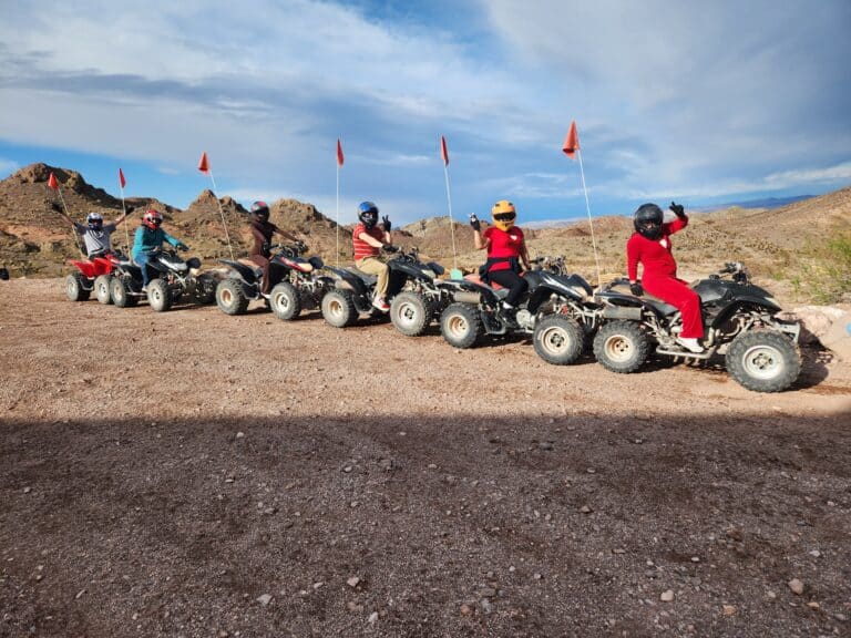 Six riders on ATVs with red flags line up on rocky Nevada terrain near Las Vegas, ready for an epic RZR off-road tour adventure.