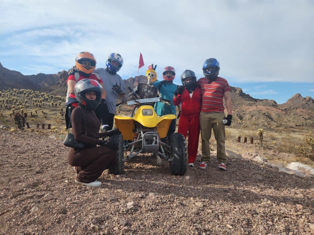 Seven adventurers in helmets pose by a yellow ATV near Las Vegas on a Nevada desert tour with Colorado River views.