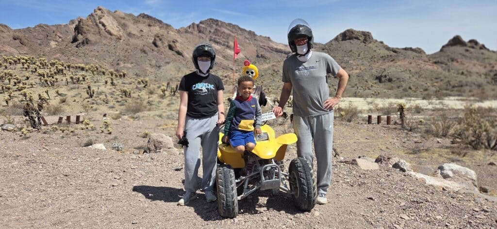 Family enjoys a Las Vegas ATV tour: two adults and a child in helmets pose by Nevada desert hills near the Colorado River.