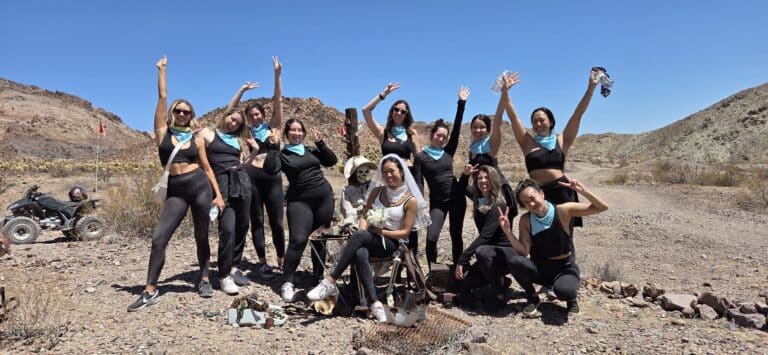 Women in black outfits and blue scarves pose in the Nevada desert near Las Vegas with dogs and ATVs—perfect for RZR off-road tours.