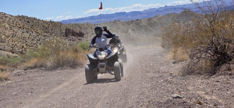 Helmeted rider waves while leading an ATV tour near Las Vegas, Nevada, with rocky trails and desert views by the Colorado River.