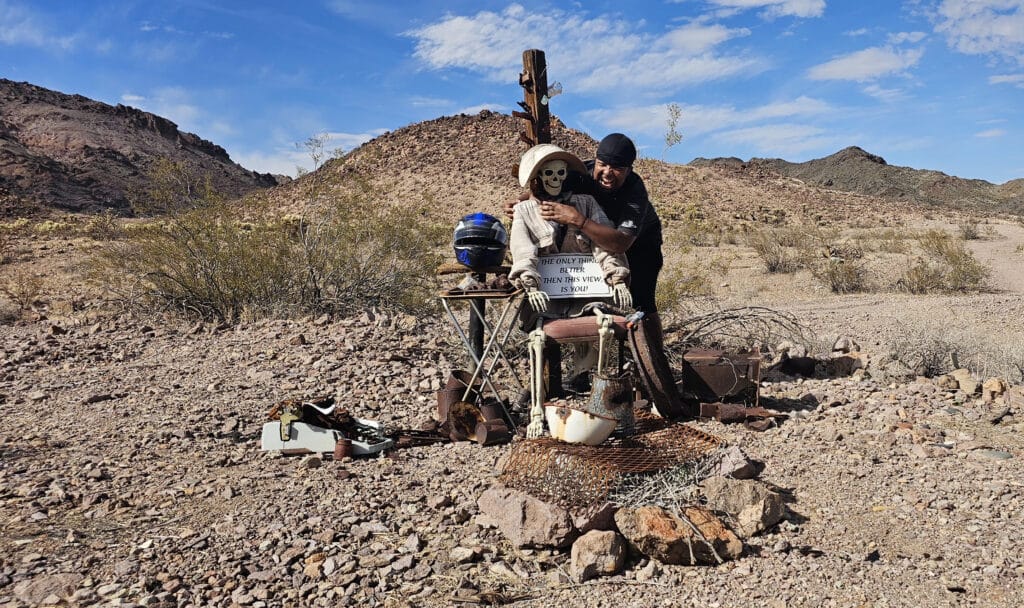 A man hugs a skeleton in sunglasses at a quirky Nevada desert setup near Las Vegas—perfect for Ghost Town sightseeing or ATV tours.