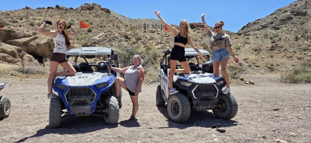 Four women enjoy a playful ATV adventure near Las Vegas, Nevada, posing by off-road vehicles amid desert hills and blue skies.