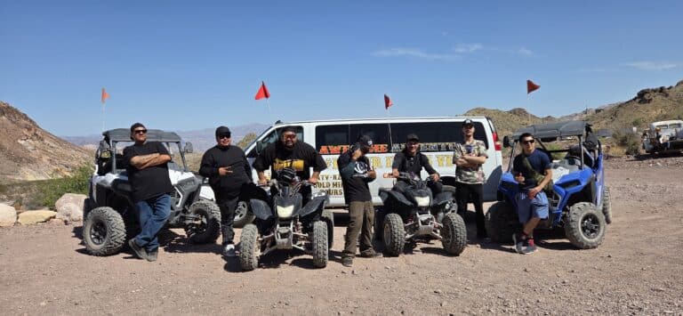 Six people pose by a white van and RZR off-road vehicles in Nevada’s desert near Las Vegas on an epic ATV tour adventure.