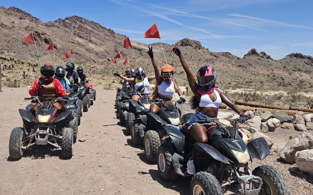 Adventure seekers in helmets ride ATVs near Las Vegas, Nevada, raising flags amid desert hills—perfect for RZR tours and Ghost Town sightseeing.