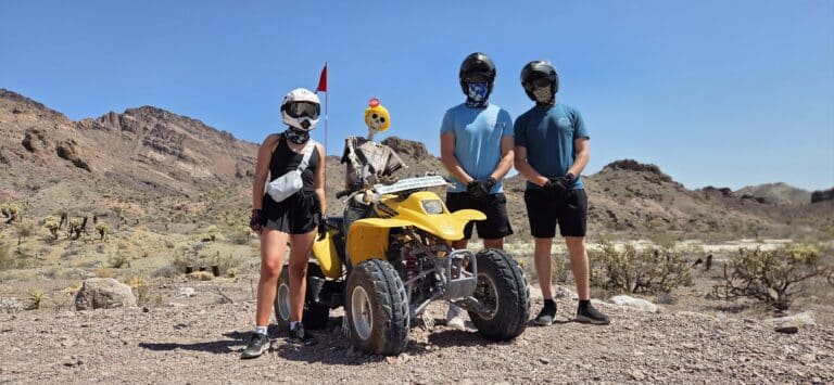 Adventurers in helmets pose by a yellow ATV near Las Vegas, Nevada, ready for an off-road RZR tour by the Colorado River.