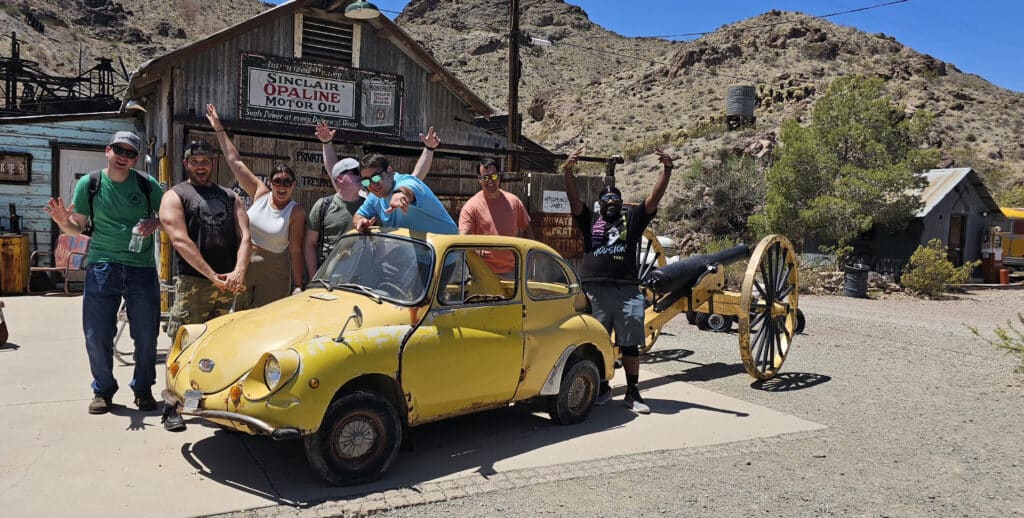 Smiling group poses by vintage yellow car and Sinclair sign at a Nevada Ghost Town near Las Vegas—perfect for sightseeing tours!.