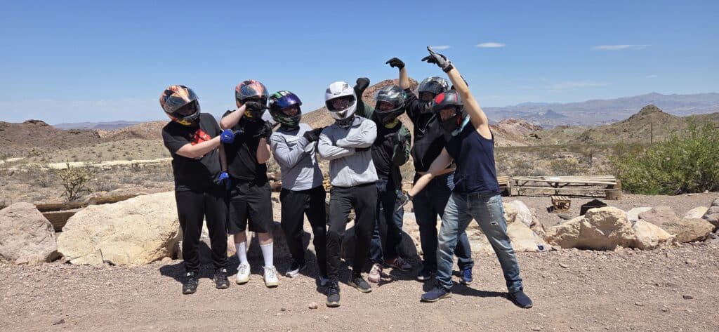 Seven adventurers in helmets pose on a Nevada desert trail near Las Vegas after an exciting RZR ATV tour by the Colorado River.