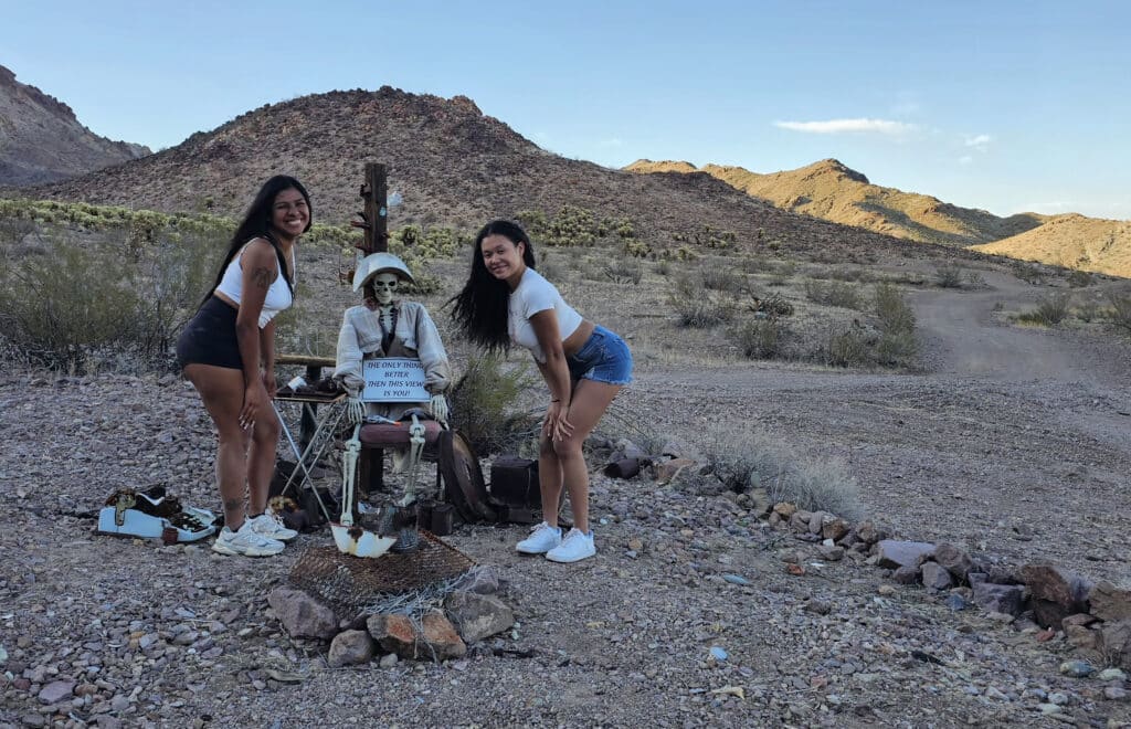 Two women smile with a skeleton prop in Nevada desert near Las Vegas on a Ghost Town sightseeing adventure.