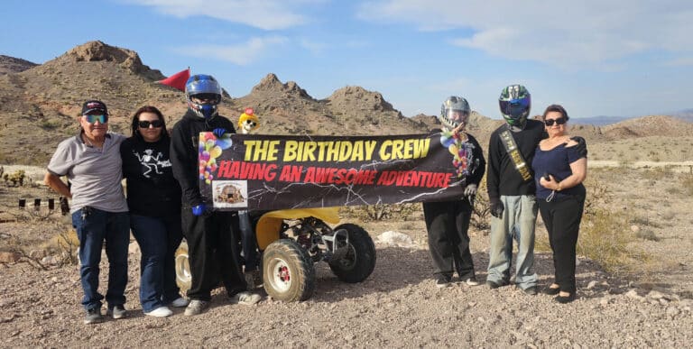 Six friends celebrate in a Nevada desert near the Colorado River, posing with an ATV on a Las Vegas RZR off-road adventure.