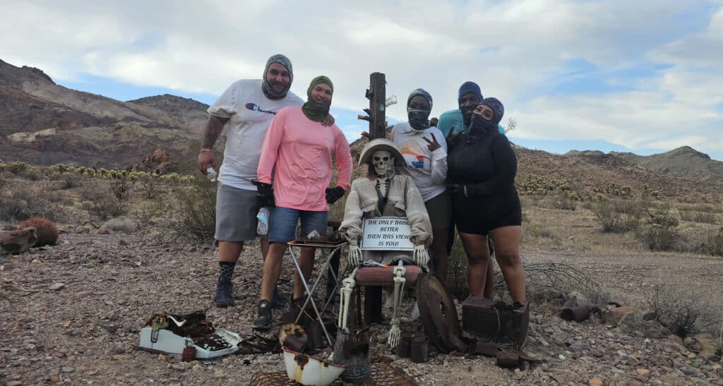 Group in desert attire poses with a miner skeleton scene near Las Vegas on a Nevada ghost town sightseeing adventure.