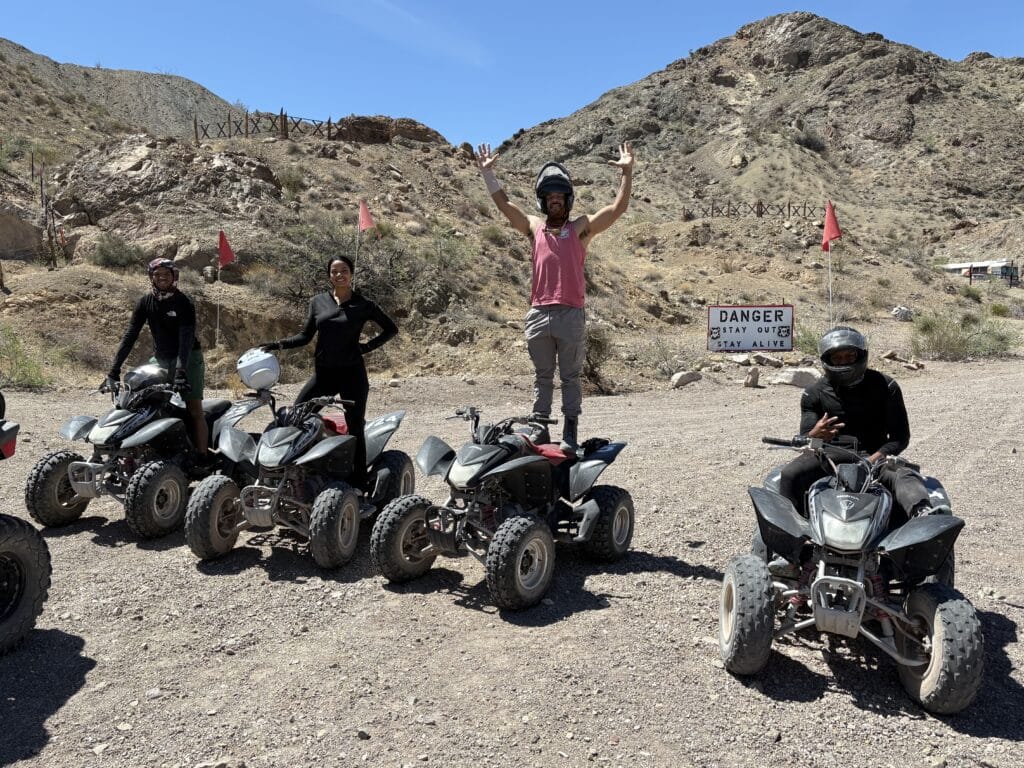 Adventure seekers on an ATV tour near Las Vegas pose in the Nevada desert with a Danger Stay Out sign and rugged hills behind.