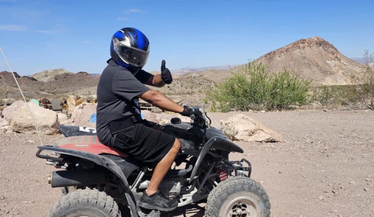 Rider in black gear on an ATV gives thumbs-up in Nevada desert near Las Vegas, with mountains and blue sky—perfect for ATV tours!.