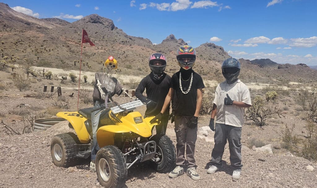 Four riders in helmets pose with a yellow ATV in Nevada’s desert near Las Vegas—perfect for ATV tours and RZR off-road adventures.