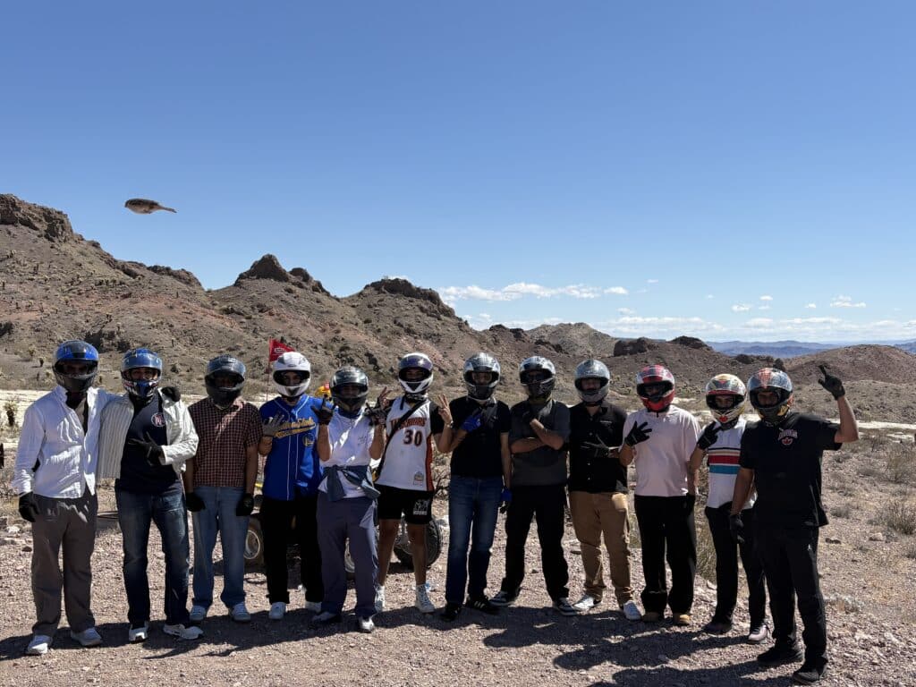 A group of 12 on an ATV tour near Las Vegas stand on rocky Nevada terrain, mountains and the Colorado River in the background.