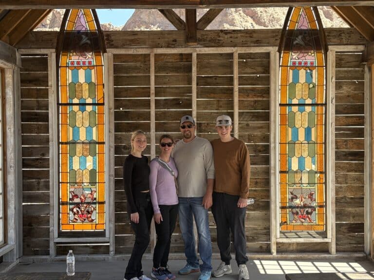 Four friends smile together in a rustic Nevada ghost town near Las Vegas, sunlight streaming through stained glass windows.
