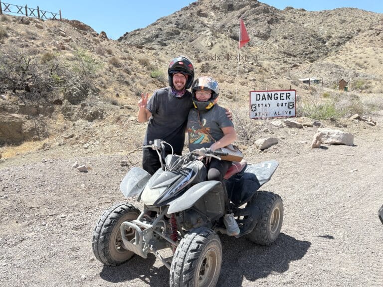 Adventurers in helmets pose with an ATV on a Nevada desert trail near Las Vegas—perfect for Colorado River RZR tours!.