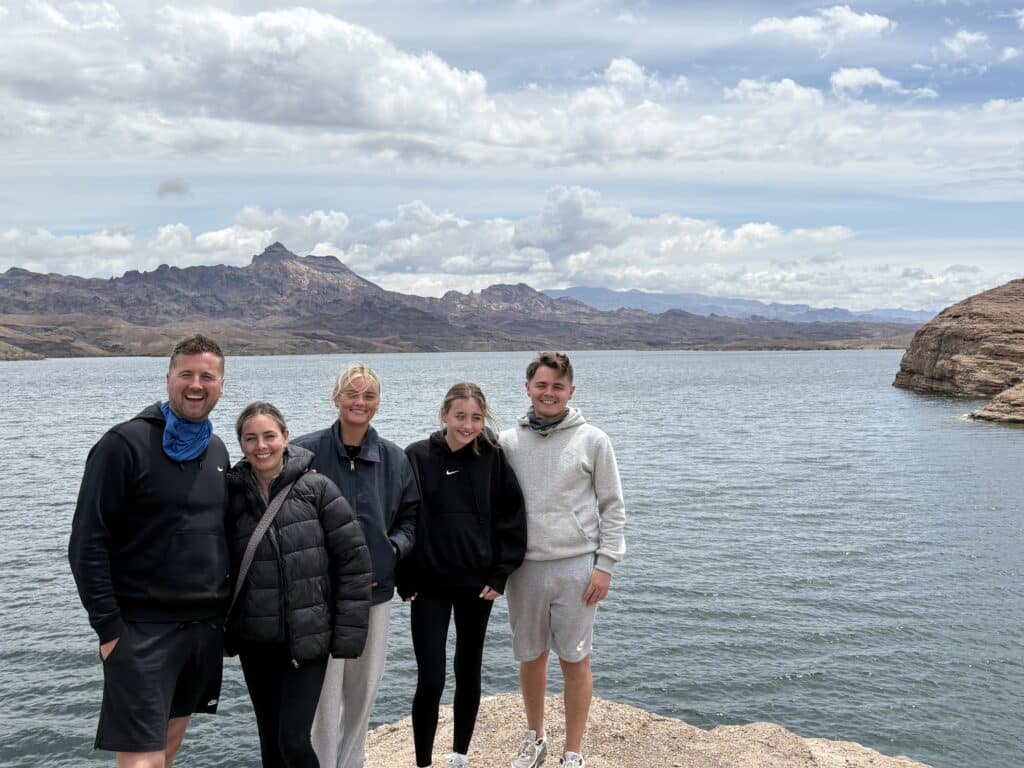 Five friends smile on the rocky shores of Nevada’s Colorado River near Las Vegas, ready for a cool-weather ATV tour adventure.