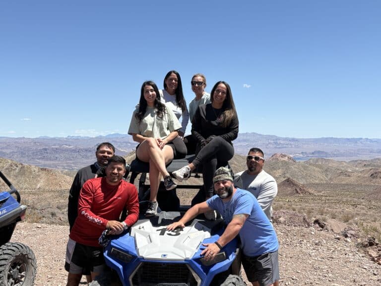Smiling group enjoys a Las Vegas ATV tour near the Colorado River with scenic Nevada mountains in the background.