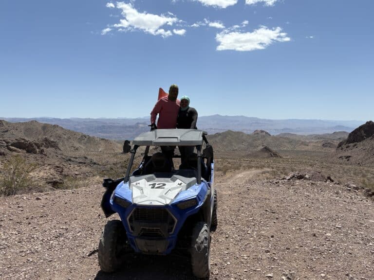 Two adventurers stand in a blue RZR on a rocky Nevada trail near Las Vegas, exploring the desert on an exciting ATV tour.