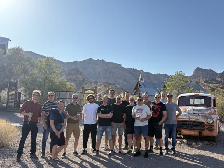 Sixteen friends pose by a vintage orange truck in a Nevada ghost town near Las Vegas and the Colorado River, enjoying sightseeing adventures.