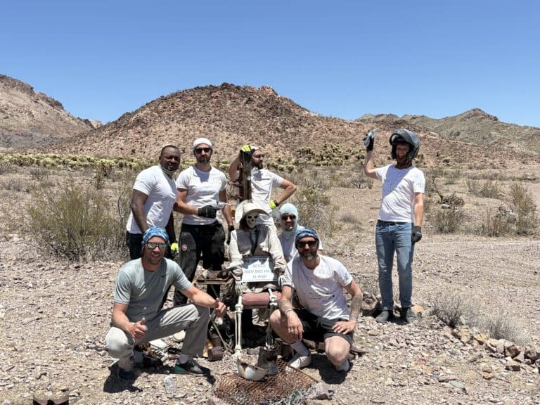 Smiling group poses by a skeleton in helmet on an ATV tour near Las Vegas, Nevada desert with Colorado River views.