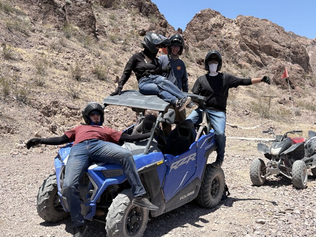 Adventurers in helmets pose on a blue Polaris RZR during a thrilling Nevada ATV tour near Las Vegas and the Colorado River.