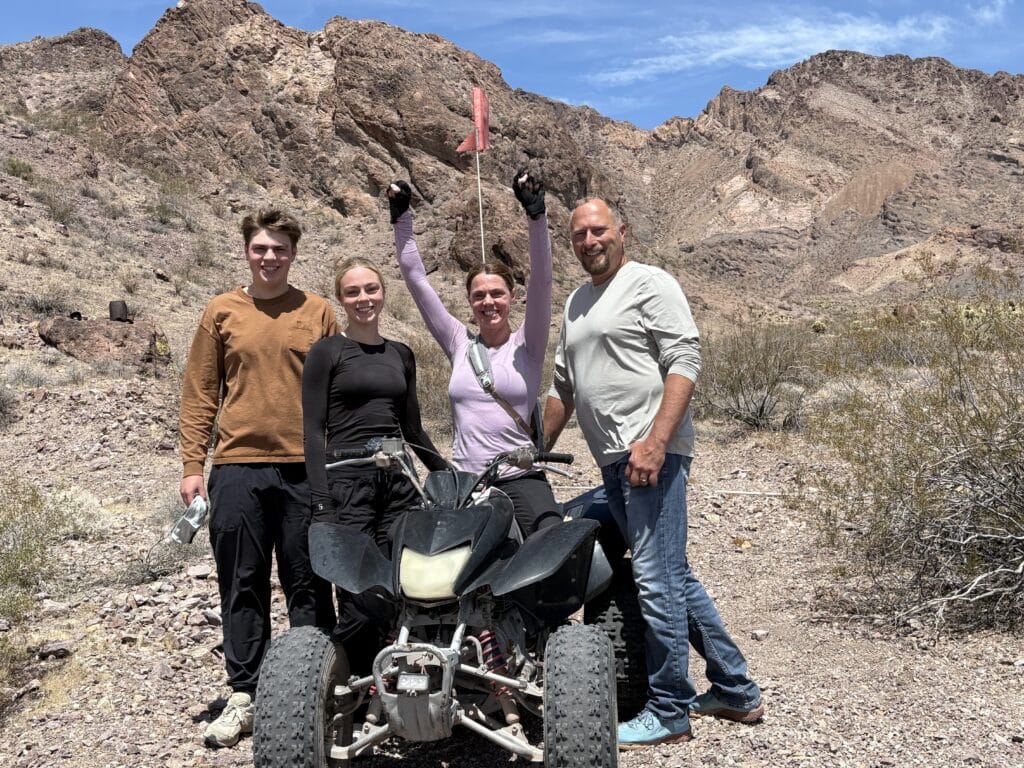 Four friends enjoy an ATV tour near Las Vegas in the Nevada desert, posing by an RZR with mountain views and sunny skies.