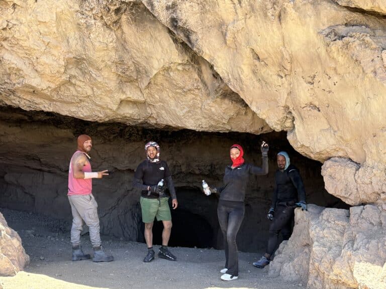 Adventurers in outdoor gear pause by a rocky cave near the Colorado River, Nevada during a Las Vegas ATV and RZR off-road tour.