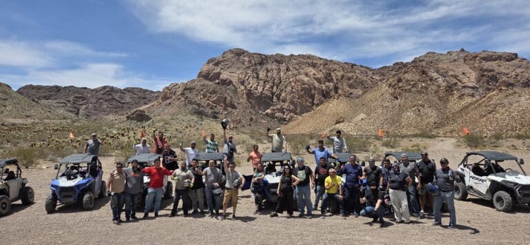 Group celebrates in front of ATVs near Nevada’s rocky mountains on a Las Vegas RZR off-road tour by the Colorado River.