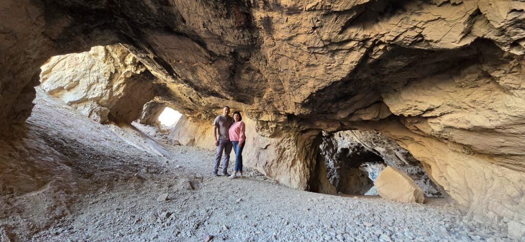 Two explore a rocky cave near Las Vegas, Nevada, with sunlight streaming in—perfect for ATV tours & Colorado River adventures nearby.