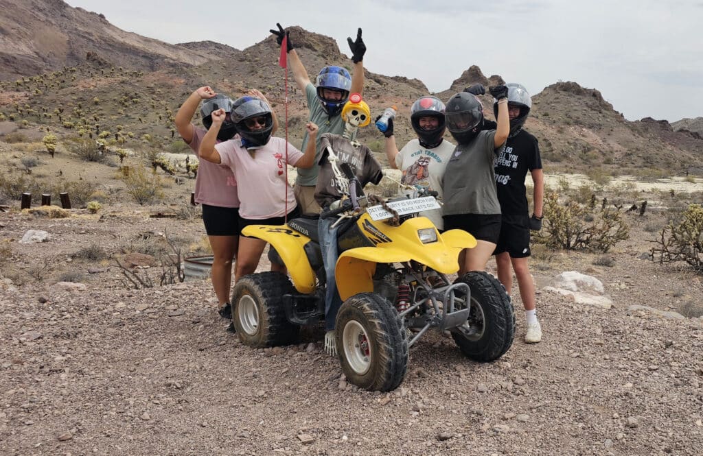 Group in helmets poses by yellow ATV amid Nevada desert near Las Vegas, perfect for RZR tours & Colorado River adventures.