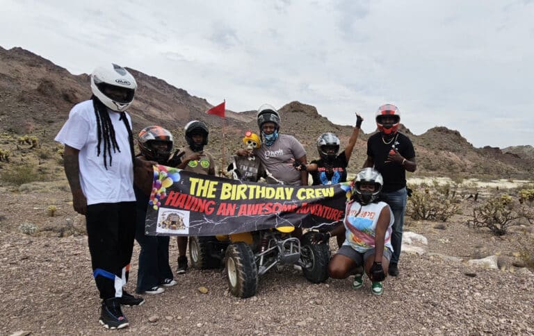 A group poses with a quad bike in Nevada’s rocky desert near Las Vegas, enjoying an ATV tour—“Birthday Crew Having an Awesome Adventure.”.
