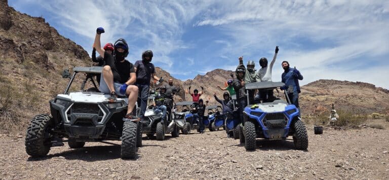 Adventurers in helmets pose on ATVs during a thrilling Las Vegas RZR off-road tour by the Colorado River in Nevada’s desert.