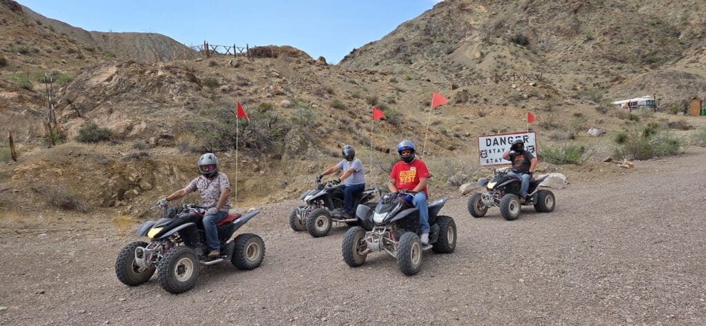 Adventure seekers enjoy an ATV tour near Las Vegas, Nevada, riding through desert trails with red flags and Danger signs in view.