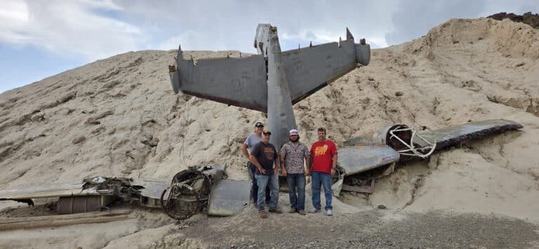 Four adventurers pose by a plane wreck in Nevada desert near Las Vegas, perfect for ATV tours and Ghost Town sightseeing.