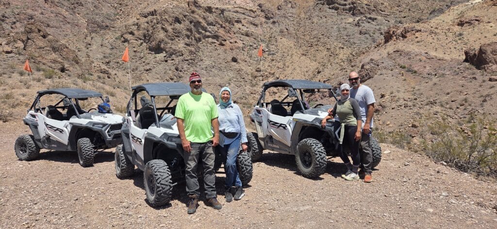 Group poses by two RZRs in Nevada’s rocky desert near Las Vegas, ready for an ATV tour along the Colorado River.